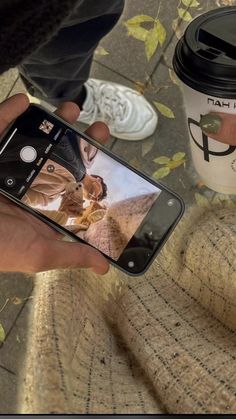 a person taking a photo with their cell phone next to a cup of coffee on the ground