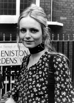 a black and white photo of a woman standing in front of a fence with a sign behind her