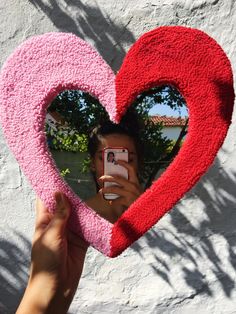 a person taking a selfie in front of a heart - shaped frame with a cell phone