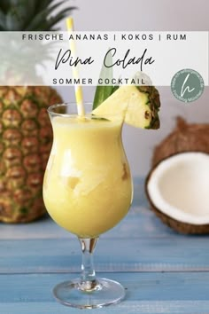 a drink in a glass with a pineapple on the side and some coconuts behind it