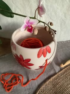 a white bowl with red flowers in it next to a yarn ball and crochet hook