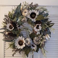 a wreath with sunflowers and greenery hanging on a white door frame in front of shutters