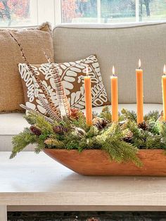 a wooden bowl filled with candles on top of a table next to a couch and pillows