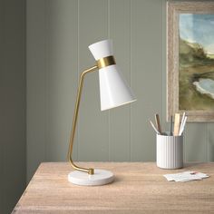 a desk lamp sitting on top of a wooden table next to a cup and pencils