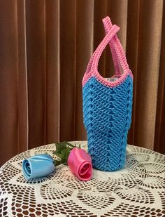 a crocheted bag sitting on top of a table next to a pink rose