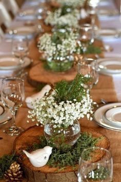 the table is set with white flowers and greenery in glass vases on wood slices