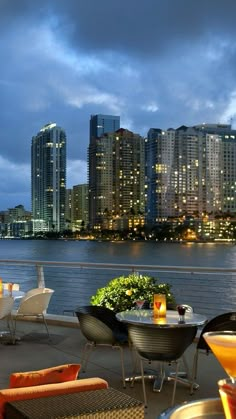 an outdoor dining area overlooking the water with city lights in the background