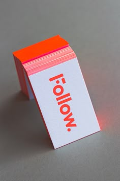 an orange and white business card sitting on top of a gray surface with the word follow printed on it