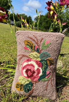 a crocheted pillow sitting in the grass with flowers on it's side