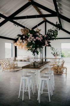 a room with tables, chairs and flowers hanging from the ceiling in front of them