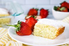 a piece of cake with powdered sugar and strawberries on the plate next to it