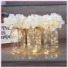 three mason jars filled with white flowers and fairy lights