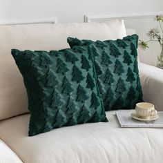 two green pillows sitting on top of a white couch next to a cup and saucer