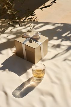 A shot of a whiskey glass accompanied by a stylishly wrapped gift box, set outdoor on a white cloth under a gentle breeze.