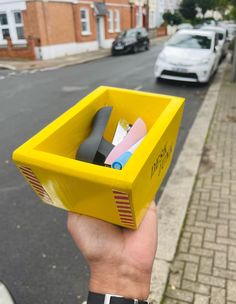 a person holding up a yellow box with scissors and other items in it on the street