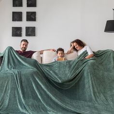 a man, woman and child sitting on a couch under a blanket