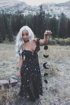 a woman with white hair and makeup is standing in a field holding a wind chime