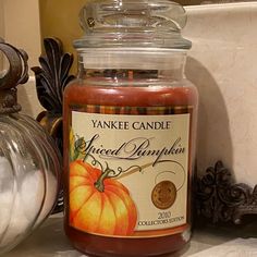 a jar of yankee candle sitting on top of a table next to pumpkins and other decorations