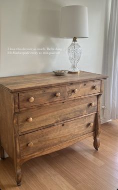 an old wooden dresser with a glass vase on it's top and a lamp on the side