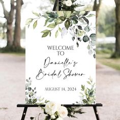 a welcome sign with greenery and white flowers is displayed in front of a path