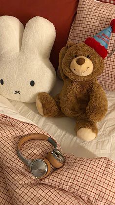 a teddy bear sitting on top of a bed next to a stuffed animal wearing a party hat