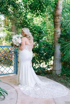 a woman in a wedding dress standing next to a tree and looking at her bouquet