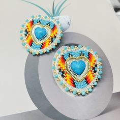 two pairs of colorful beaded heart shaped earrings on top of a circular object with a white background