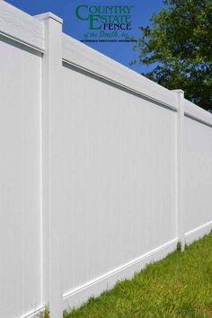 a white vinyl fence with grass and trees in the background