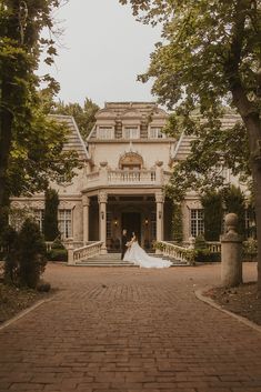 a bride and groom are standing in front of a large house with trees on either side