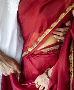 a woman wearing a red sari with gold accents on her chest and hand in the pocket