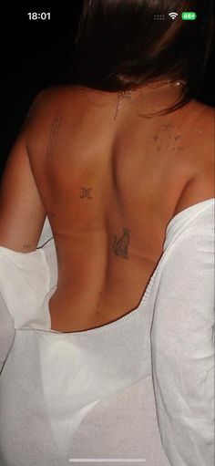 the back of a woman's white shirt with tattoos on her upper and lower chest