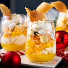 two glasses filled with fruit and ice cream on top of a white plate next to christmas ornaments