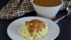 a white plate topped with mashed potatoes covered in gravy next to a bowl of gravy