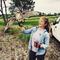 a woman holding an owl in her right hand and smiling while standing next to a truck