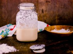 a glass jar filled with liquid next to two spoons on top of a wooden table