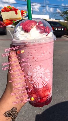 a person holding up a drink with whipped cream and strawberries on it, in front of a parking lot