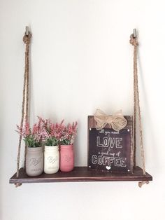 two hanging shelves with flowers and coffee mugs on them in front of a white wall