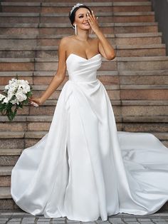 a woman in a white wedding dress standing on some steps with her hand to her face