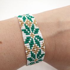 a woman's arm wearing a green and white beaded bracelet with gold beads