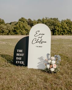 a white and black grave marker with flowers on it in the middle of a field