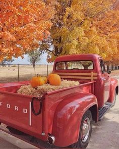 an old red truck with hay and pumpkins in it's flatbed bed