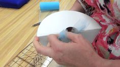 a person is cutting paper with scissors on a wooden table next to a wire basket