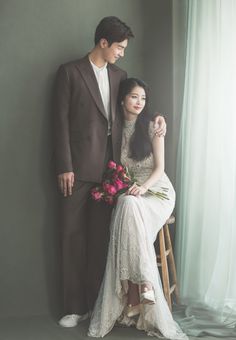 a man and woman sitting next to each other in front of a window holding flowers