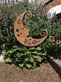 a metal moon and stars sitting on top of a planter in front of purple flowers