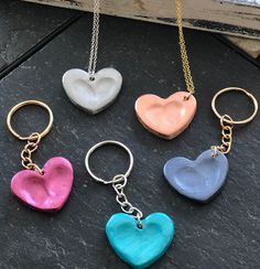 four different colored heart shaped key chains on a black stone surface with a gold chain