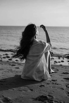 a woman sitting on top of a sandy beach next to the ocean with her arms in the air