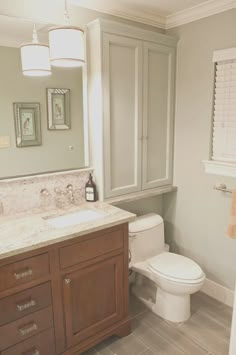 a white toilet sitting next to a sink in a bathroom under a mirror and cabinet