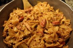 a bowl filled with pasta and meat on top of a table next to a wooden spoon