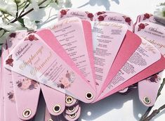 pink and gold wedding fan with flowers on the table next to each other in front of white flowers