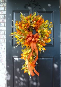 a wreath with orange and yellow flowers is hanging on the front door's black door